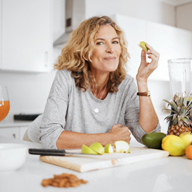 Woman smiling while snacking on fruit in kitchen