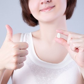 Woman holding her extracted tooth and making thumbs-up gesture